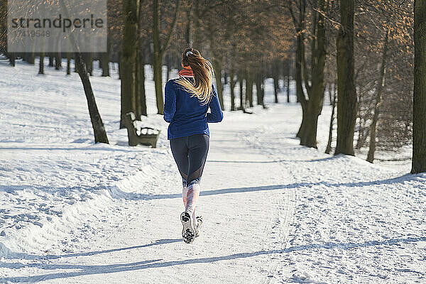 Frau joggt im Winter bei Schnee auf Fußweg