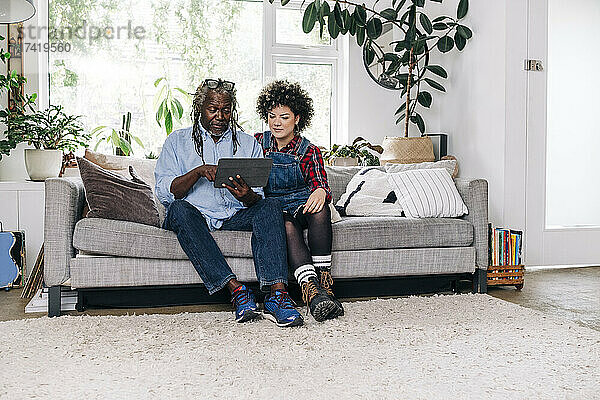 Älterer Mann benutzt digitales Tablet  während er mit seiner Tochter auf dem Sofa sitzt