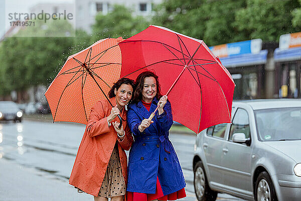 Glückliche Freundinnen mit Regenschirm  die mit dem Auto auf der Straße unterwegs sind