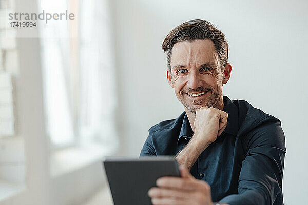 Lächelnder männlicher Profi mit digitalem Tablet am Arbeitsplatz