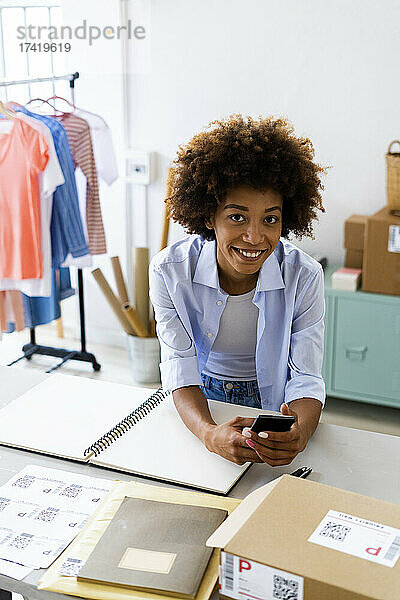 Junge Modedesignerin mit Smartphone im Studio