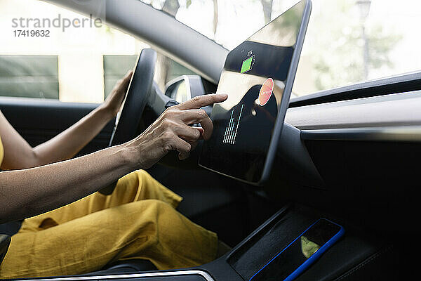 Frau nutzt digitales Tablet beim Fahren eines Elektroautos