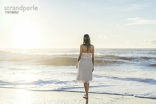 Braut blickt auf den Sonnenaufgang  während sie am Strand steht