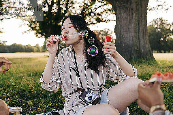 Frau bläst Seifenblasen  während sie mit Freunden im Park sitzt