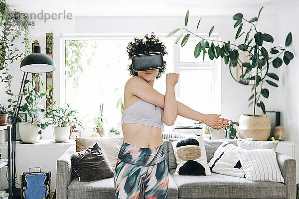 Junge Frau mit Virtual-Reality-Headset dehnt sich zu Hause