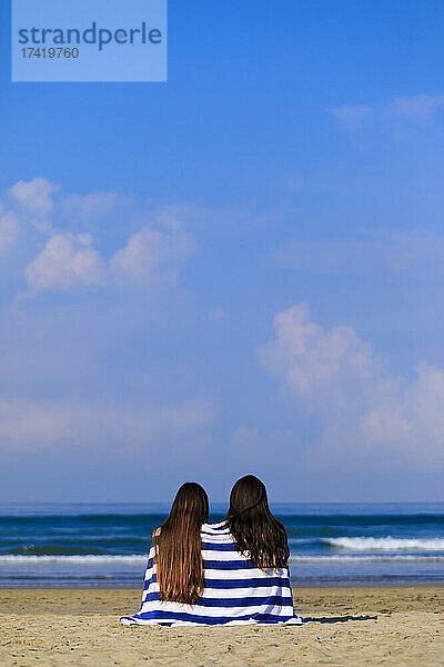 In Handtücher gehüllte Frauen sitzen an sonnigen Tagen am Strand