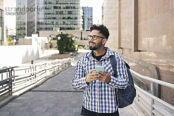 Lächelnder Mann mit Handy und Rucksack in der Stadt