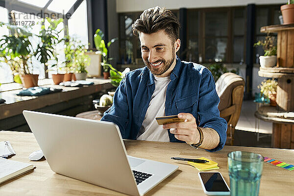 Männlicher Berufstätiger mit Kreditkarte beim Online-Shopping im Büro