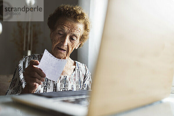 Ältere Frau liest Brief  während sie zu Hause mit Laptop sitzt