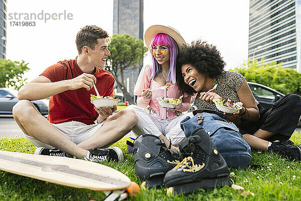Fröhliche junge multiethnische Freunde essen Salat im Park