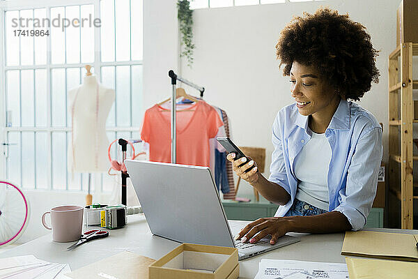 Modedesignerin mit Laptop und Mobiltelefon während der Arbeit im Studio