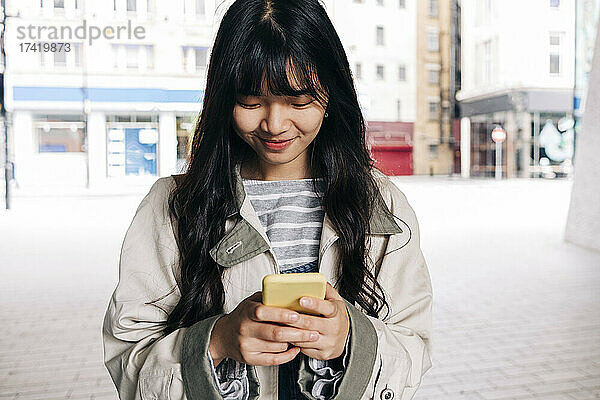 Lächelnde Frau  die SMS über ihr Smartphone in der Stadt sendet