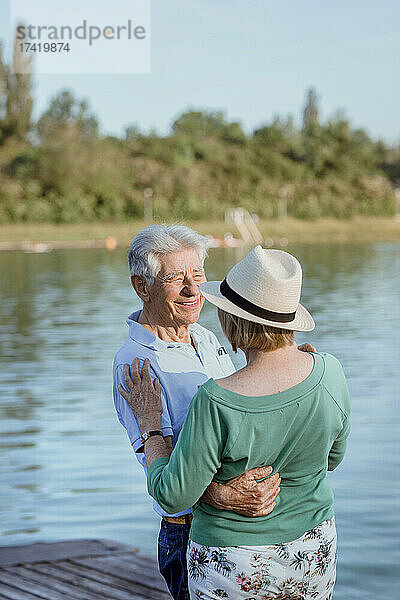 Älterer Mann schaut Frau mit Hut auf Steg am See an