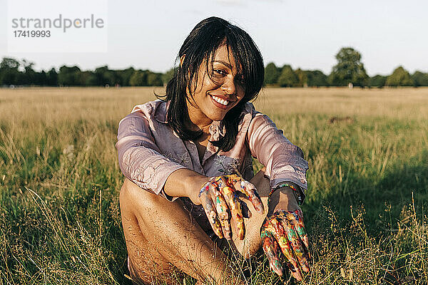 Lächelnde Frau mit Farbe auf den Händen  die an einem sonnigen Tag im Park sitzt