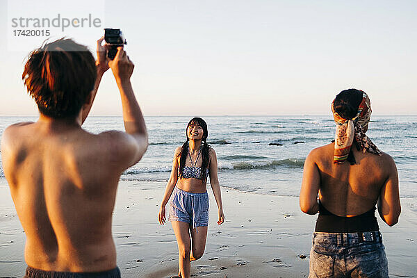 Junger Mann fotografiert Freundin am Strand