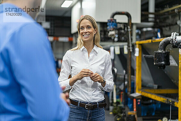 Lächelnde Geschäftsfrau diskutiert mit Kollegen  während sie in der Fabrik steht