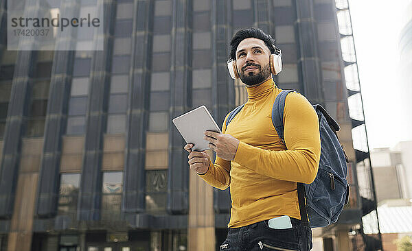 Schöner Mann  der in der Stadt Musik hört und ein digitales Tablet in der Hand hält
