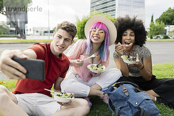 Mann macht Selfie mit Freundinnen  die Salat im Park halten