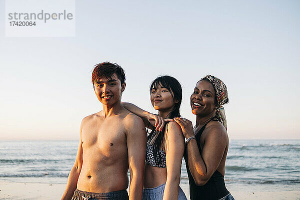 Lächelnder Mann mit Freundinnen  die bei Sonnenuntergang am Strand stehen