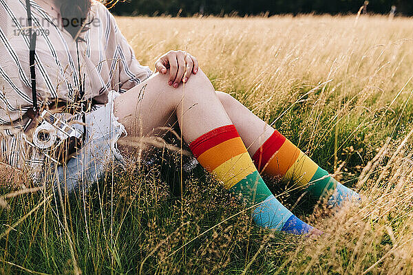 Frau mit Kamera und Regenbogensocken sitzt auf Gras