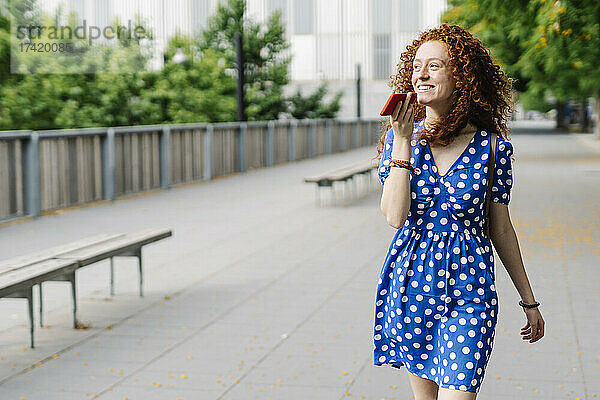 Lächelnde Frau sendet Voicemail per Mobiltelefon  während sie auf dem Fußweg geht