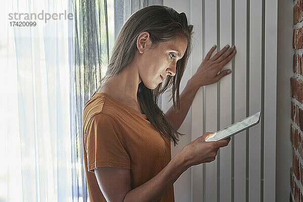 Frau überprüft zu Hause die Temperatur des Heizkörpers über ein digitales Tablet