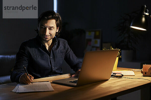 Geschäftsmann unterschreibt Dokument  während er zu Hause spät abends am Laptop arbeitet