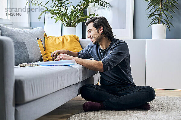 Männlicher Student lernt  während er zu Hause einen Laptop benutzt