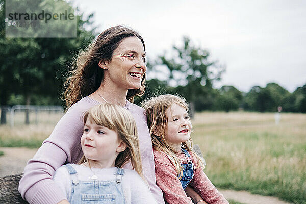Lächelnde Mutter sitzt mit Töchtern im öffentlichen Park