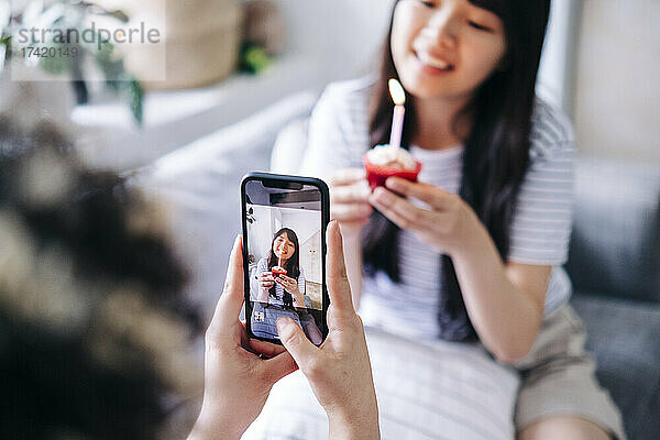 Frau fotografiert Freundin mit Cupcake zu Hause über Smartphone