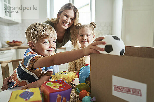 Lächelnder Junge legt Spielzeug in Spendenbox  Familie im Hintergrund zu Hause