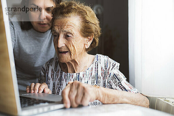 Enkelin hilft Großmutter  während sie zu Hause Laptop benutzt