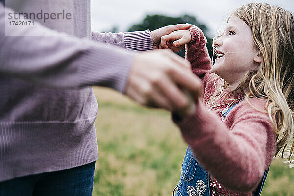 Lächelnde Tochter hält die Hände der Mutter beim Spielen im Freien