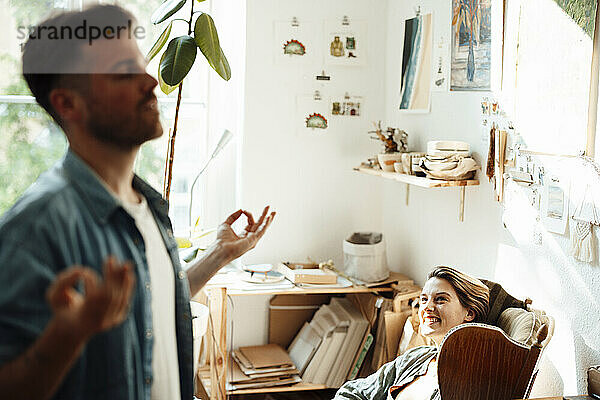 Lächelnde Frau blickt Mann beim Meditieren zu Hause an