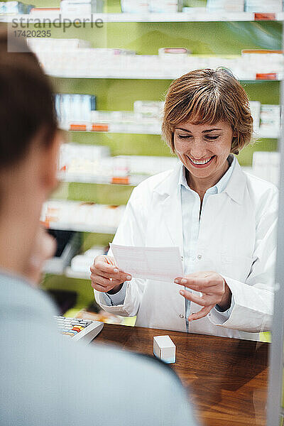 Lächelnder Apotheker liest das Rezept  während er mit dem Kunden im Geschäft steht