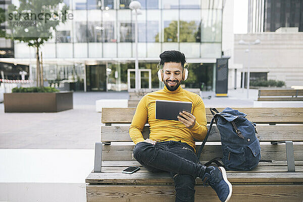 Mann schaut sich Videos über ein digitales Tablet an  während er auf einer Bank sitzt