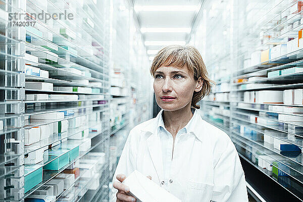 Apothekerin mit Medikamenten schaut weg  während sie am Regal im Sanitätshaus steht