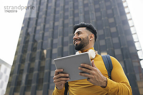 Lächelnder Mann hält digitales Tablet vor Wolkenkratzer