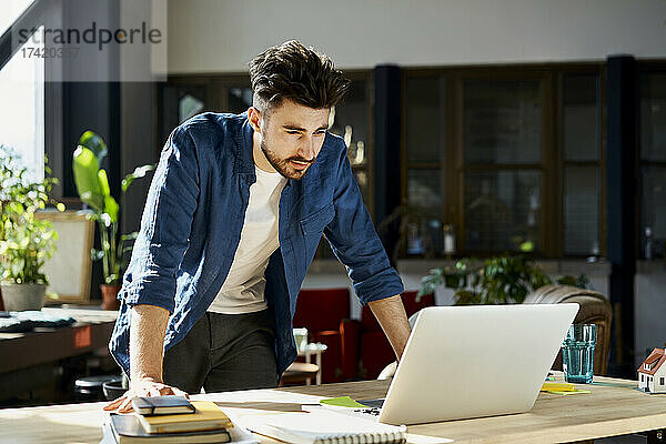 Junger Geschäftsmann schaut im Büro auf Laptop