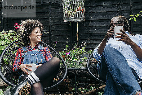 Lächelnde Frau mit Kaffeetasse spricht mit Mann  während sie im Hinterhof sitzt
