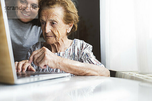 Lächelnde junge Frau hilft Großmutter mit Laptop zu Hause
