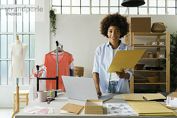 Modedesignerin mit Laptop und Umschlag im Studio