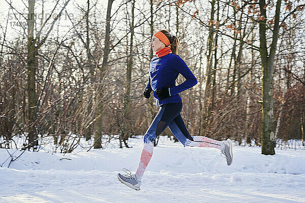 Frau läuft im Winter bei Schnee in der Nähe kahler Bäume