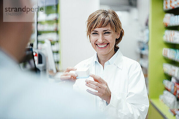 Lächelnde Apothekerin diskutiert mit männlichem Kunden in der Apotheke