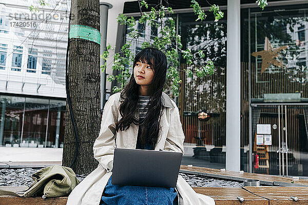 Junge Frau mit Laptop sitzt vor dem Gebäude