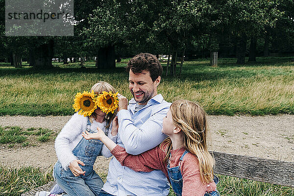 Vater bedeckt Gesicht eines Mädchens mit Sonnenblumen  während er im Park spielt