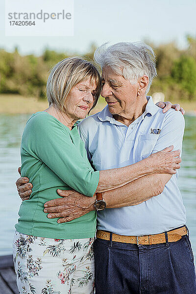 Älteres Paar mit geschlossenen Augen umarmt sich am See