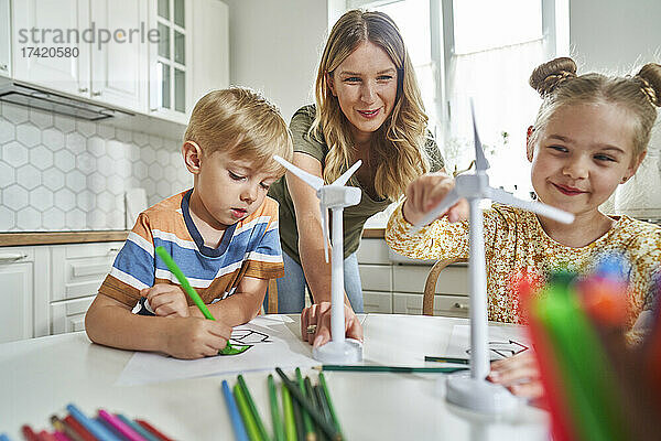 Mutter unterrichtet Kinder am Tisch über das Modell einer Windkraftanlage