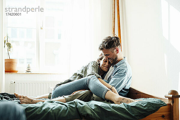 Glückliches Paar umarmt sich  während es zu Hause im Bett sitzt