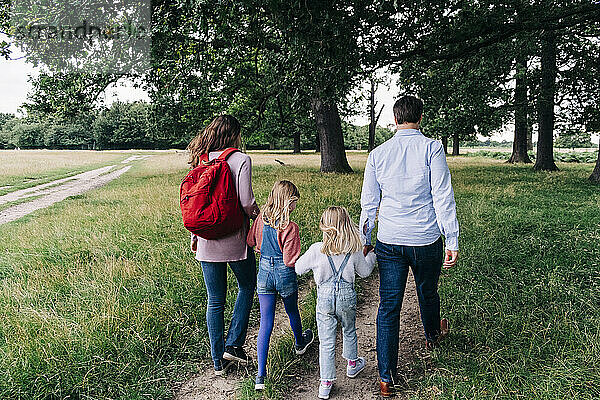 Töchter halten ihre Eltern an den Händen  während sie im Park spazieren gehen